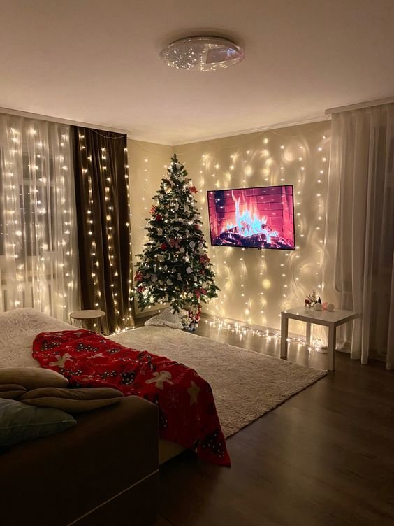 Cozy living room filled with Christmas decorations, featuring a decorated tree, string lights, and a fireplace on the TV screen.